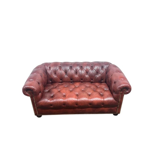 A luxurious tufted leather chesterfield sofa in a burgundy / brick red. The sofa has nicely rolled arms, boasts brass...