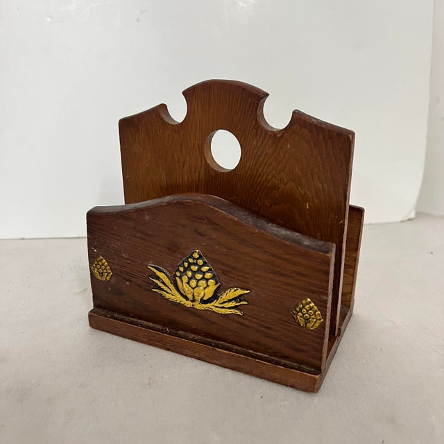 Mid Century wooden letter napkin holder embellished with brass artichokes. Measures 6” w x 4” d x 5” h.