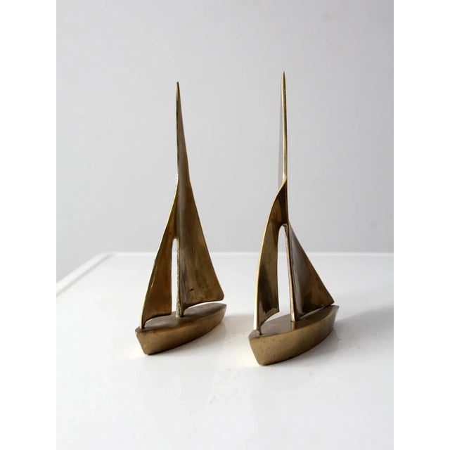 This is a pair of mid 20th century brass sailboats. The set includes a large and smaller boat with variance in the "wind"...