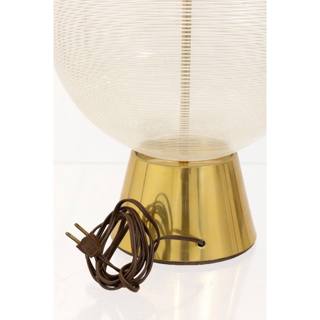This table lamp combines mid century charm with artisanal craftsmanship, featuring a clear threaded glass sphere that...