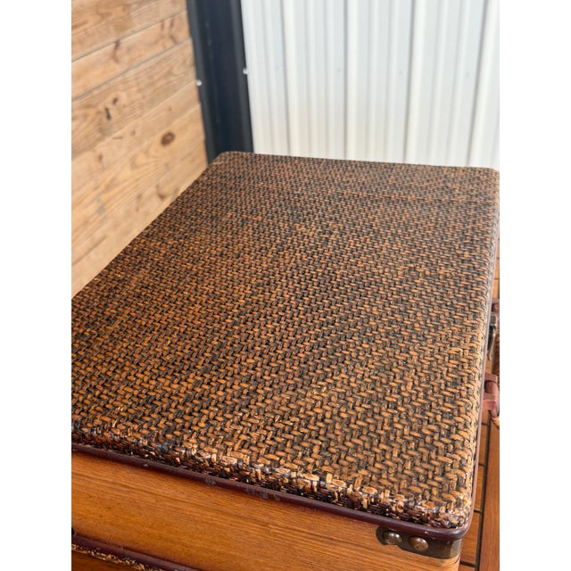 A wonderfully charming vintage decorative suitcase trunk featuring woven rattan panels, warm wood construction, brass-tone...