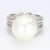 This is a large 18k white gold cocktail ring with a 14mm round pearl sat atop the ring while the accent diamonds seemingly...