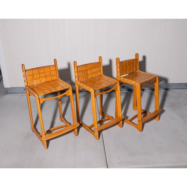 A distinctive set of three handcrafted oak counter stools by John M. Toy, each bearing the maker's branded stamp. These...