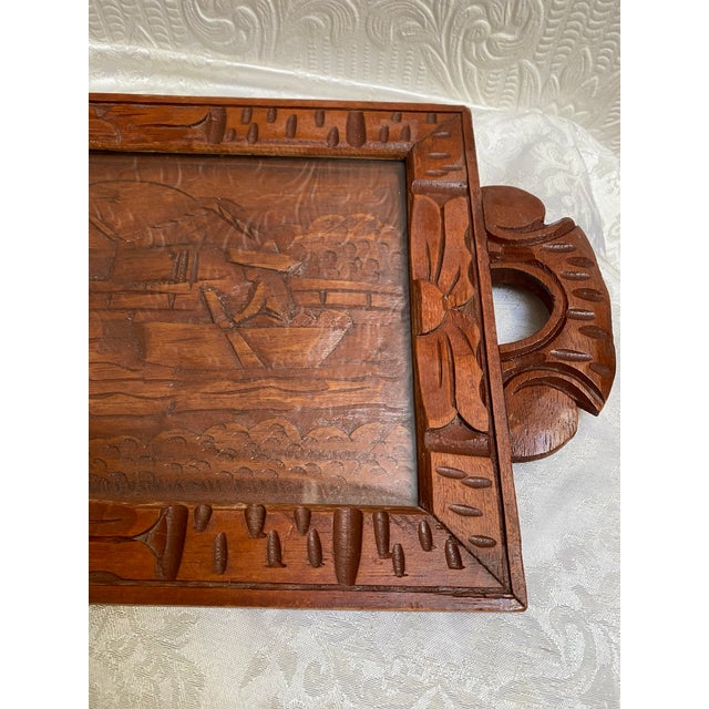 A one of a kind hand carved wooden tray depicting a man wearing a sombrero in a boat on a lake near a village, just...
