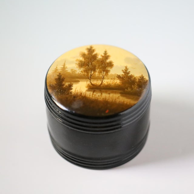 Vintage Soviet Fedoskino lacquer box of round form, hand-painted with a landscape showing water, trees, grasses, and...