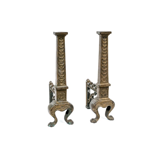 A pair of tall brass fireplace andirons with fluted, egg-and-dart carved columns, floral rosette medallion base, cabriole...