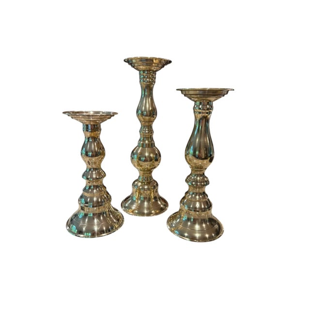 Offering a polished set of three polished brass candlestick holders. Each holder offers a unique central columns that is...