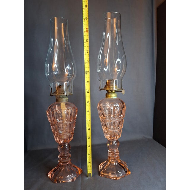 Presenting a stunning, authentic matching pair of vintage pink pressed glass kerosene lamps. These elegant lamps feature a...