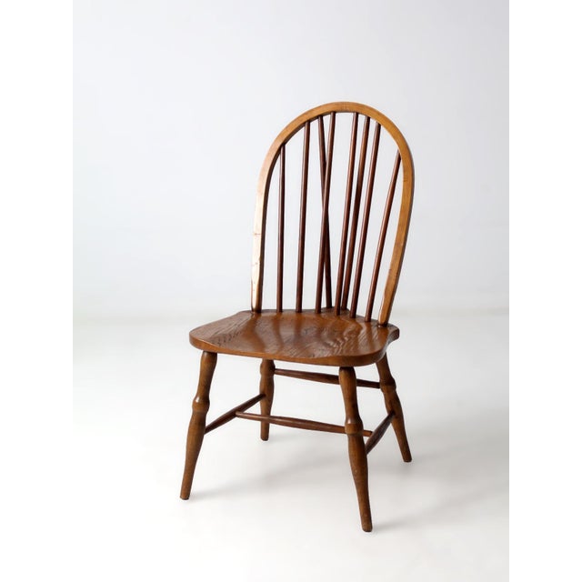 Vintage brace-back Windsor chair in the Colonial Revival style, featuring a continuous bow back with slender spindles and...