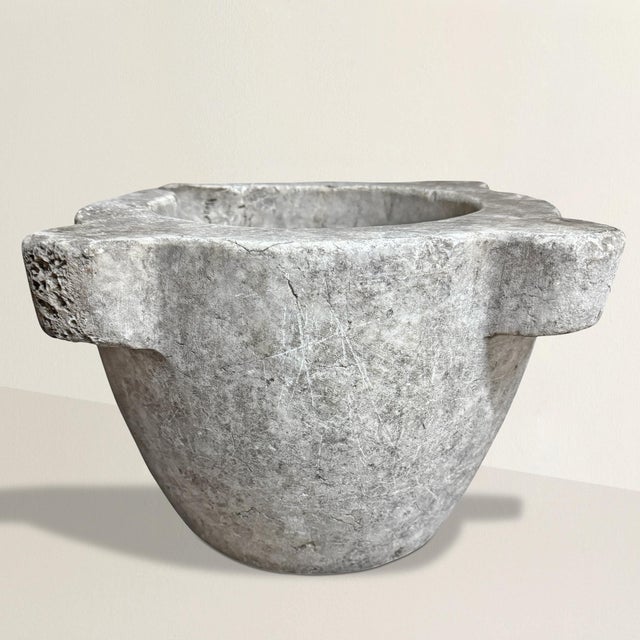 An 18th-century French carved marble mortar, rich with history and softened by centuries of use, its surface worn smooth...