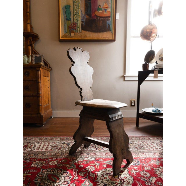 Primitive hand-carved wood chair with a scroll-cut silhouette back and a plank seat, raised on shaped, splayed trestle...
