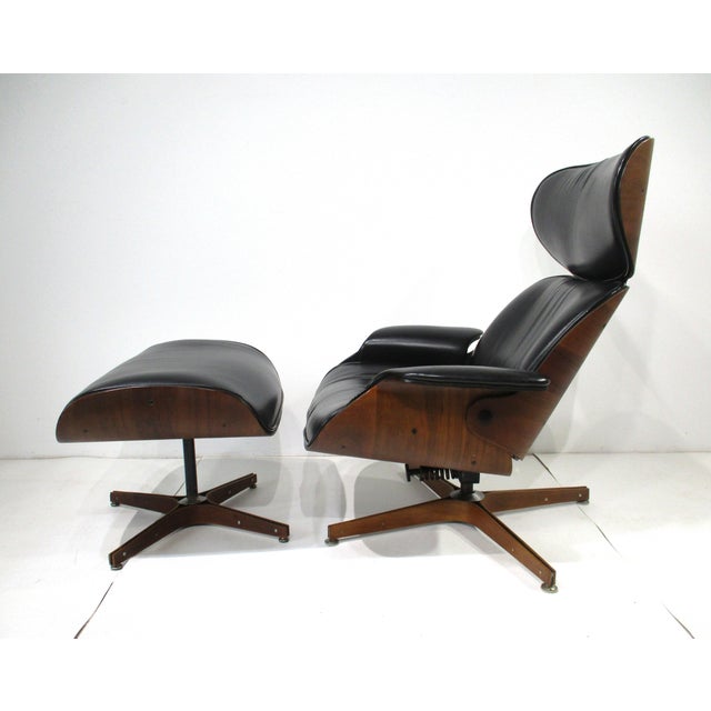 A Mid Century black leatherette and walnut swiveling high back lounge chair with matching ottoman. Each base has a...