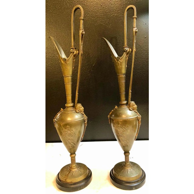 Pair of Classical figurative bronze neoclassical ewers, 19th-early 20th century. Each depicting Grecian woman water...