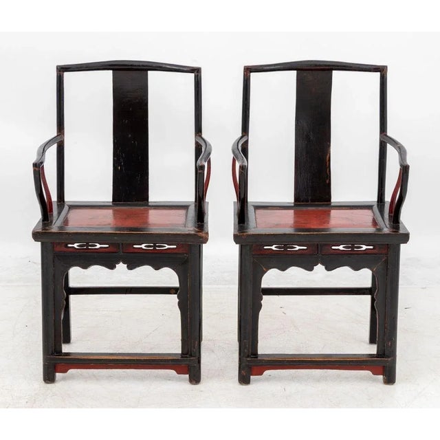 Pair of Chinese Black Lacquered Armchairs, circa 1900, with red painted seat and carved apron conjoined by box stretcher....