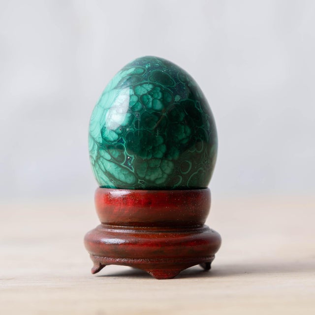 Hand-carved malachite egg with bold banding on fitted wooden stand, c.1980. Egg: 2 in tall x 1 ½ in wide; with stand: 2 ½...
