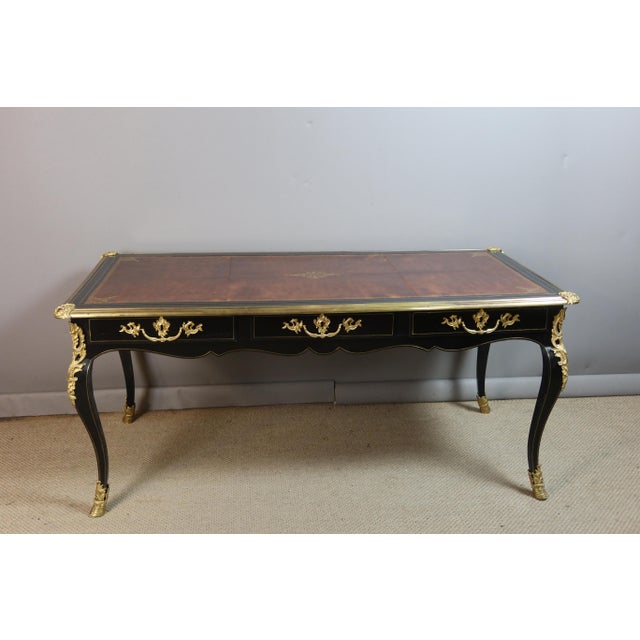 A louis xv style flat desk in ebonized wood with beautiful gilt bronze ornamentation. It rests on four cabriole legs...