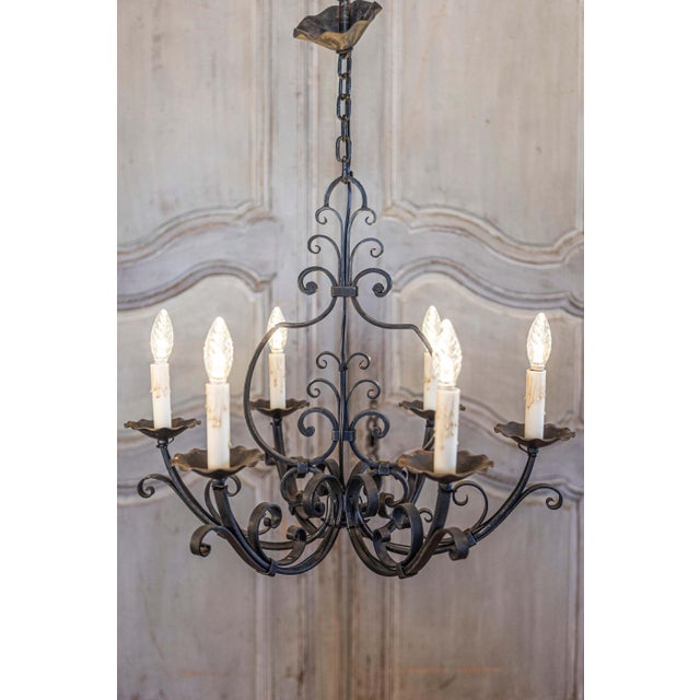 A French wrought iron chandelier from the 20th century with six lights and scrolling motifs, professionally rewired for...