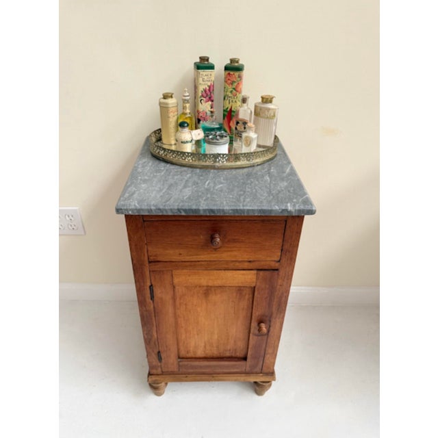 This petite antique side table brings together the warmth of aged wood and the quiet elegance of a marble top. The base is...