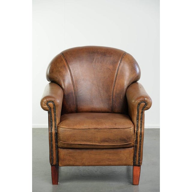 This vintage sheepskin armchair features a beautiful patina and is finished with decorative nails. The armchair has a...