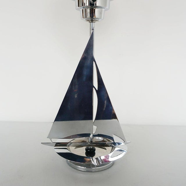 An deco table lamp. Chromed metal stem in the shape of a sailboat with a chromed riveted base and a white glass globe...