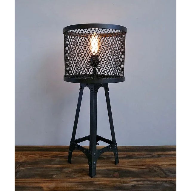 Industrial style table lamp with heavy duty iron frame with studs and iron mesh barrel lampshade. Antiqued black finish.