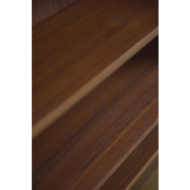 This modernist narrow book cabinet was manufactured in Sweden during the 1960. It was finished in teak and has three move...