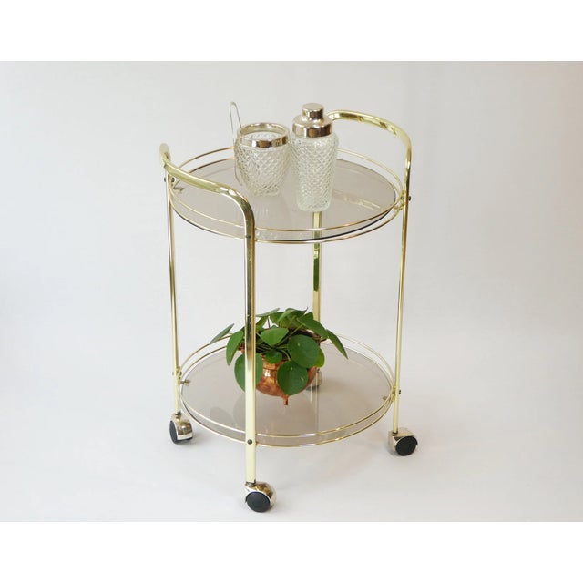 Wonderful hollywood regency brass trolley with smoked glass. It has two tiers and 4 wheels that can be easily rolled to...