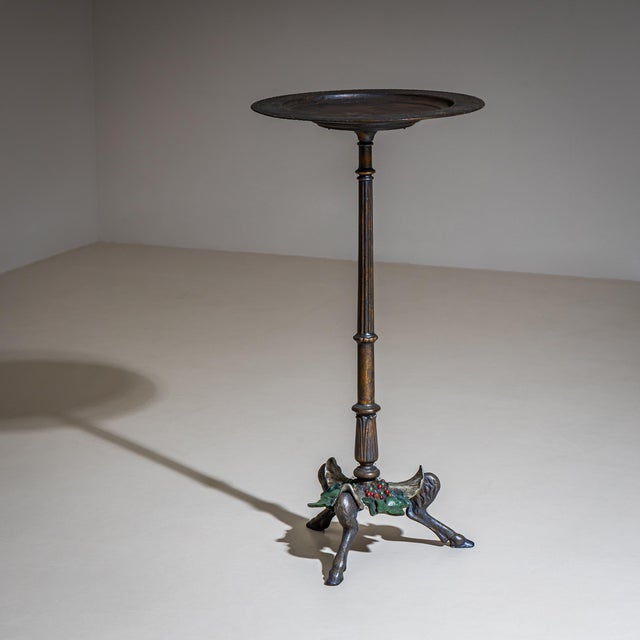 Small iron gueridon with dish-shaped top featuring a wide, relief-decorated rim and smooth center. The top rests on a...