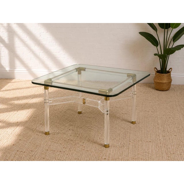A glamorous vintage gaming table combining clear Lucite, warm brass accents, and a substantial glass top. The transparent...