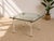 A glamorous vintage gaming table combining clear Lucite, warm brass accents, and a substantial glass top. The transparent...