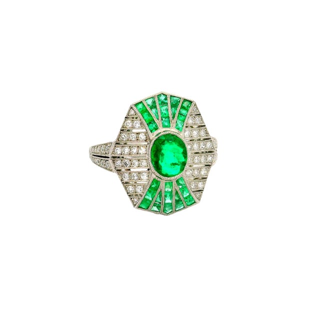 A striking and elegant art-deco inspired ring showcasing a vibrant green emerald as the centerpiece. The emerald are cut...