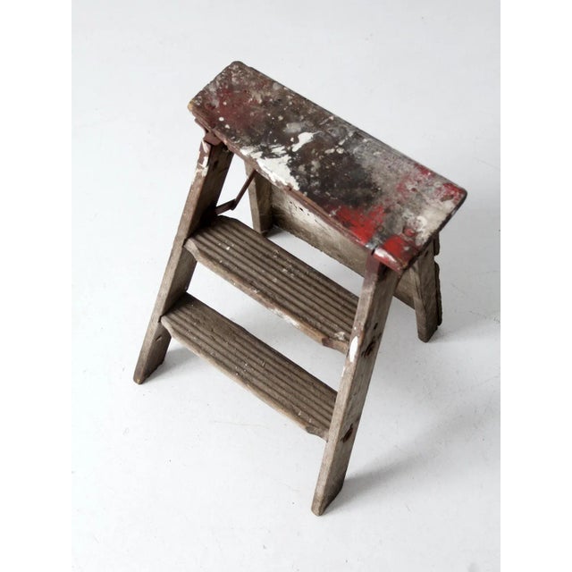 This is a vintage wooden step ladder. The rustic ladder features two rung steps with a wooden board back brace and metal...
