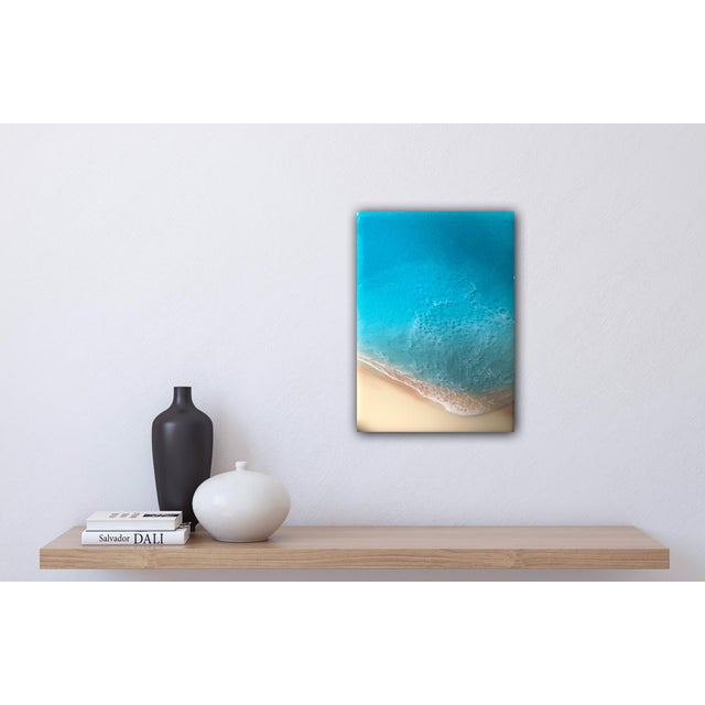 This artwork presents a serene view of a white sand beach, captured through layered resin on a wood panel. The smooth,...