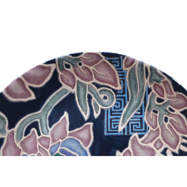 A round ceramic platter made by Toyo. The bold floral and chinoiserie pattern “Cymbaline in Lapiz” was designed by fabric...