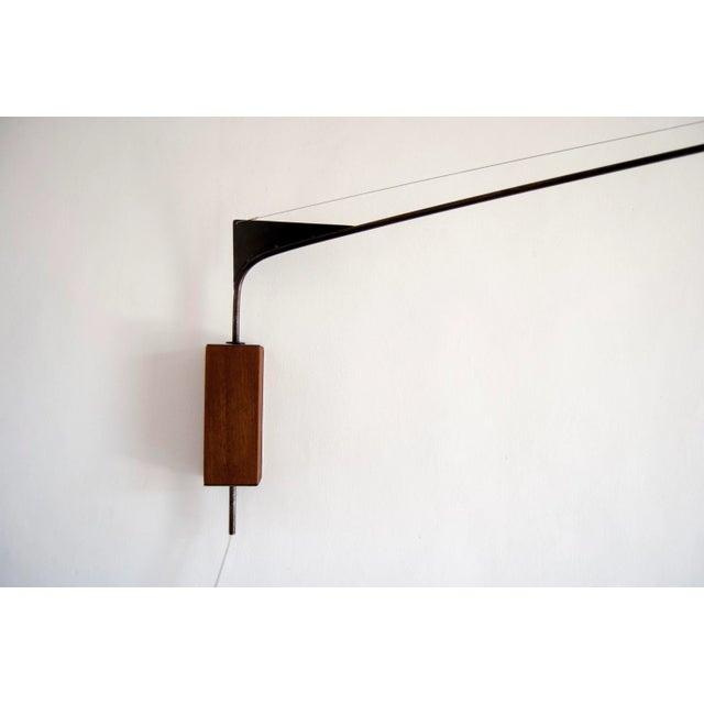 This swiveling wall lamp with a hidden wall fixing system is made of iron and iroko wood with a perforated metal shade....
