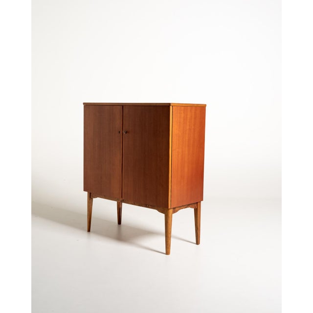 Teak cabinet with two doors, shelves, and internal drawers, raised on tapered legs. Original Ferdinand Lundquist,...