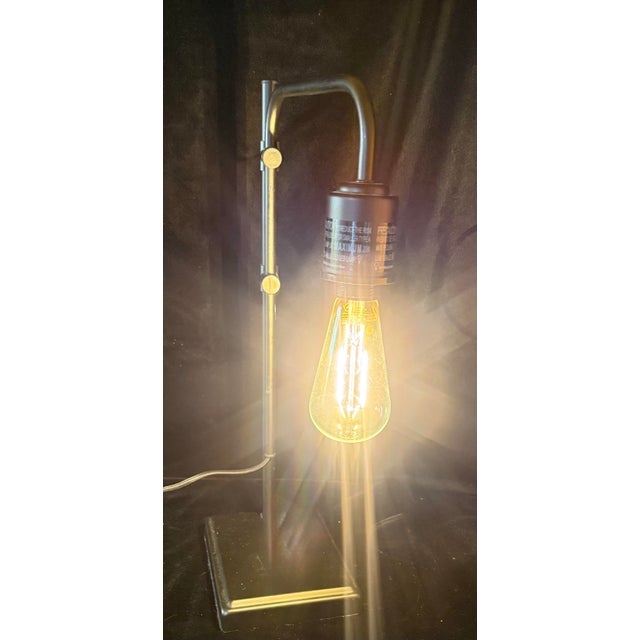 This minimalist table lamp features an industrial aesthetic with vertical metal post and an adjustable swing arm design...