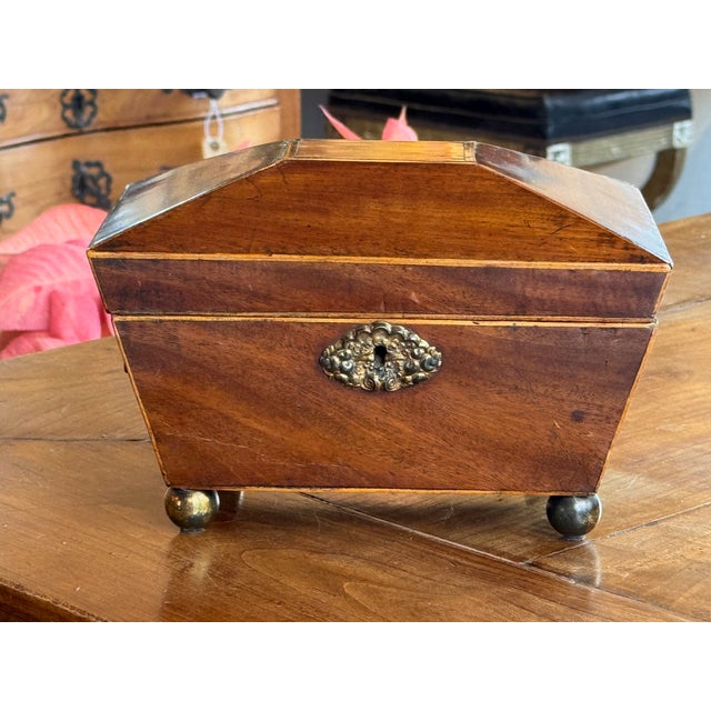 Small mahogany tea caddy of rectangular form with a hinged, faceted lid outlined by simple line inlay. The lid opens to a...