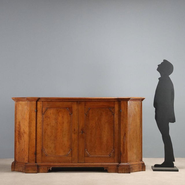 Baroque walnut sideboard with a rounded shape. Front with a pair of paneled doors, three drawers added later. Bracketed...