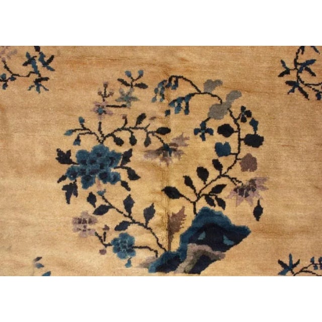 An antique Chinese Peking rug with multiple circular botanical motifs on a champagne field, surrounded by a contrasting...