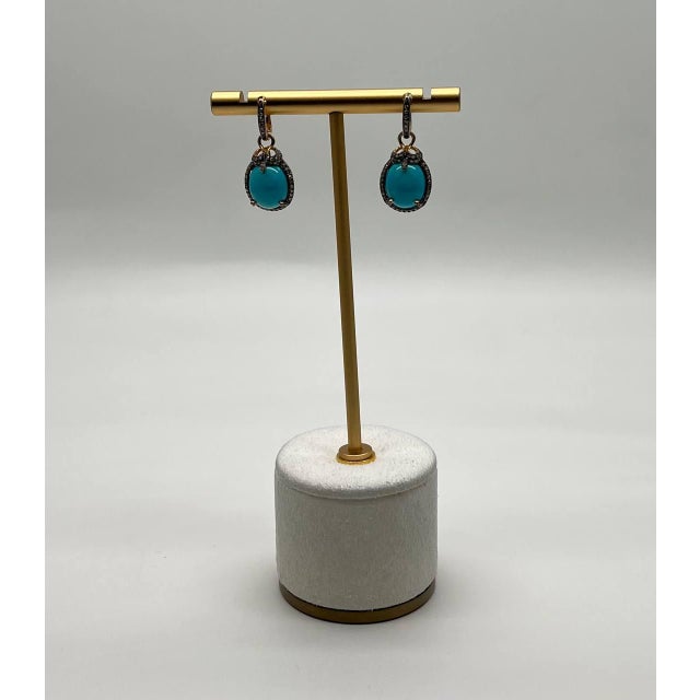 A striking pair of earrings, each featuring a vibrant turquoise stone, encased in a delicate halo of small, sparkling...