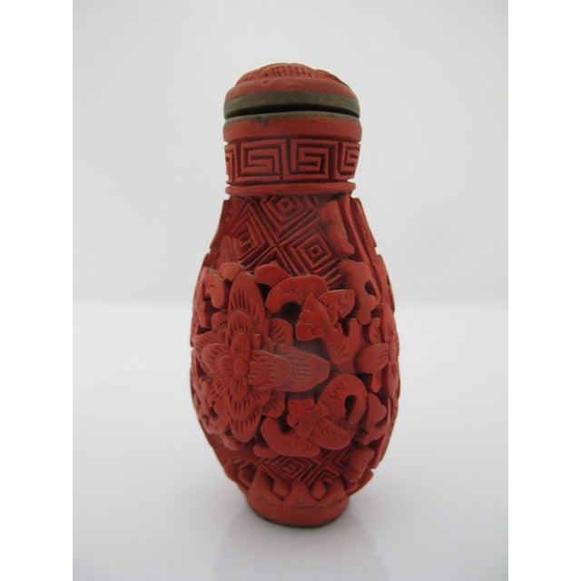 Vintage Chinese carved red cinnabar snuff bottle with a fitted brass-lined top, featuring an intricate floral motif and...