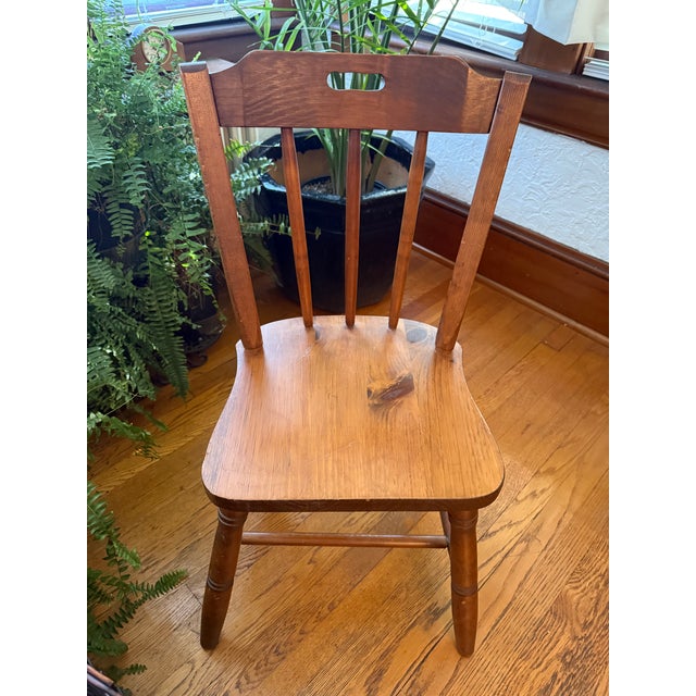 Wooden side chair with a spindle back and a solid saddle seat. Three turned spindles rise to a wide top rail with a cutout...
