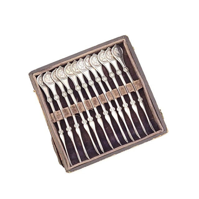A set of twelve Reed & Barton medallion nut picks in sterling. Listed measurements are for an individual utensil; the...