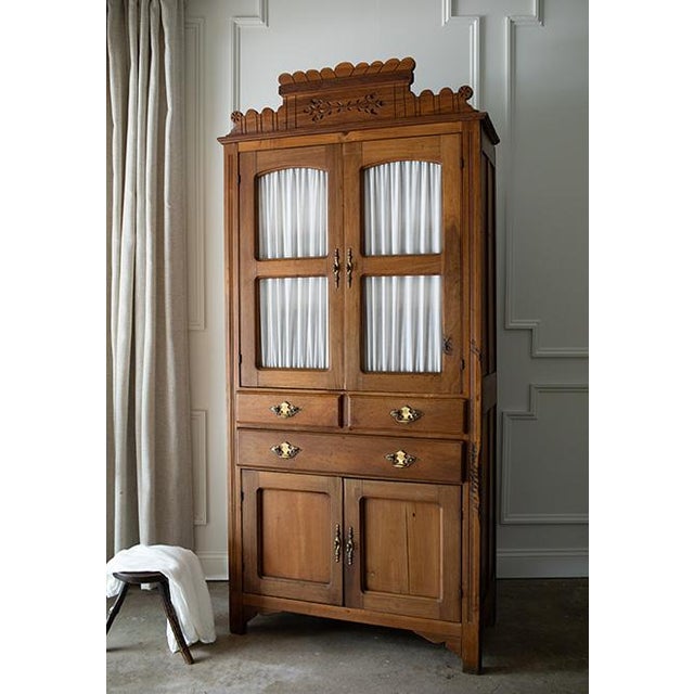 An authentic, solid wood country cabinet featuring a hand-carved scalloped crest, gathered fabric upper doors with no...
