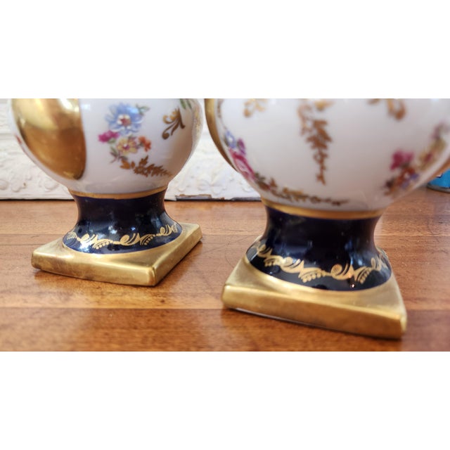 A charming small-scale pair of covered urns in the Sèvres / Louis XVI-revival manner — deep cobalt blue banding, raised...