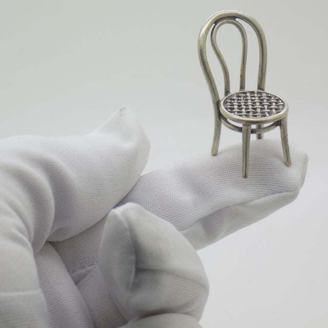 This vintage silver decorative object depicts a traditional rustic chair with a woven straw seat miniature, crafted as a...