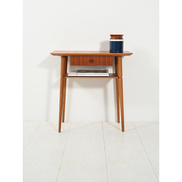 Scandinavian teak bedside table from the 1960s, slender and light, with a suspended drawer and elegantly tapered turned...