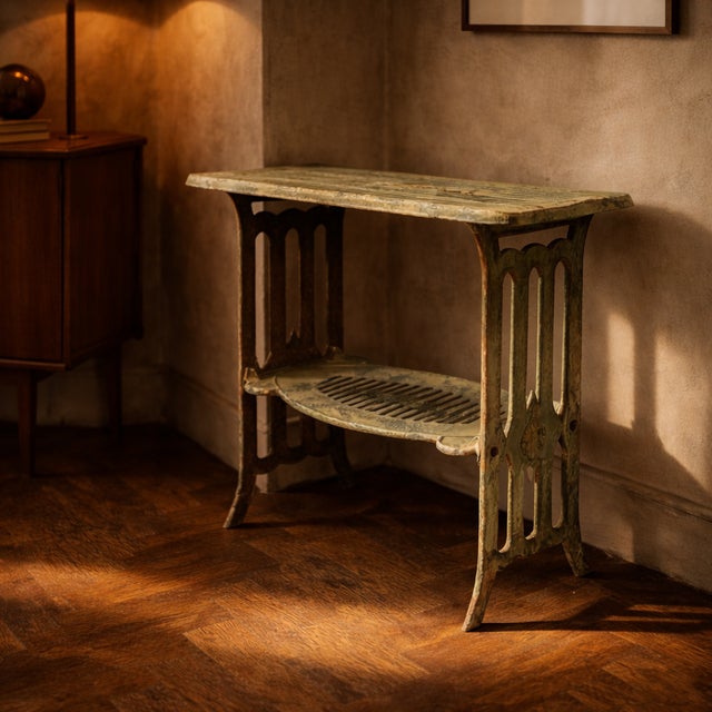 A compact metal table with a distinctive open cut-out and integrated lower shelf, combining function with an architectural...