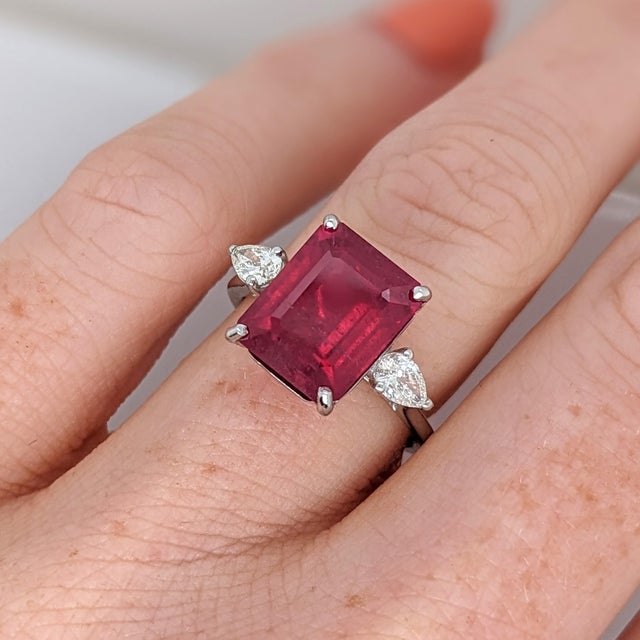 A ruby takes center stage in a vivid red at the center of this solid 14K white gold ring, surrounded by two earth-mined...